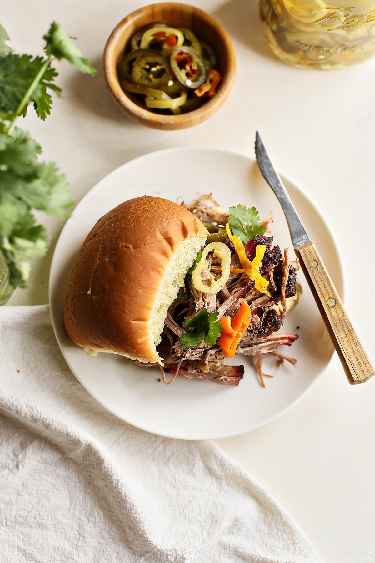 smoked pork shoulder sandwich on a white plate with a knife