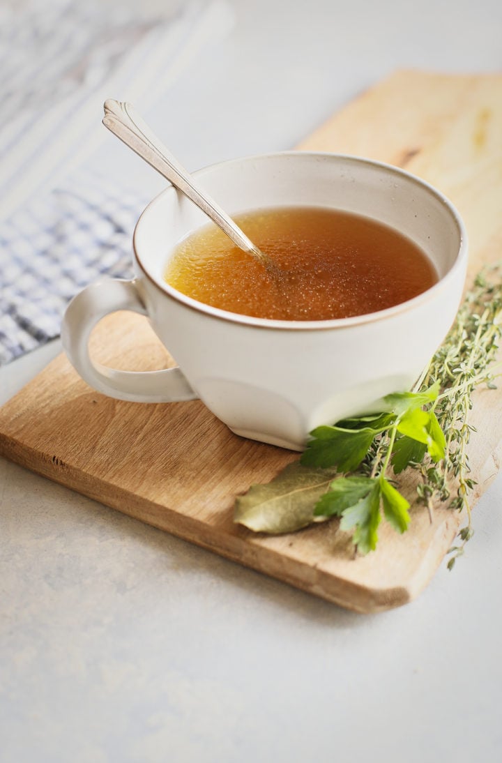 homemade Instant Pot chicken stock in a white mug with a spoon