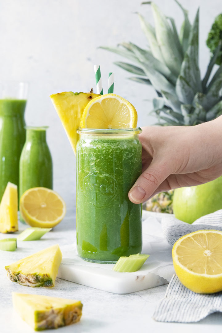 woman picking up a glass of green kale pineapple smoothie