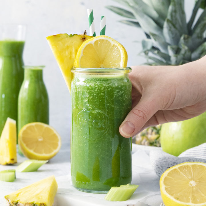 woman picking up a glass of pineapple kale smoothie