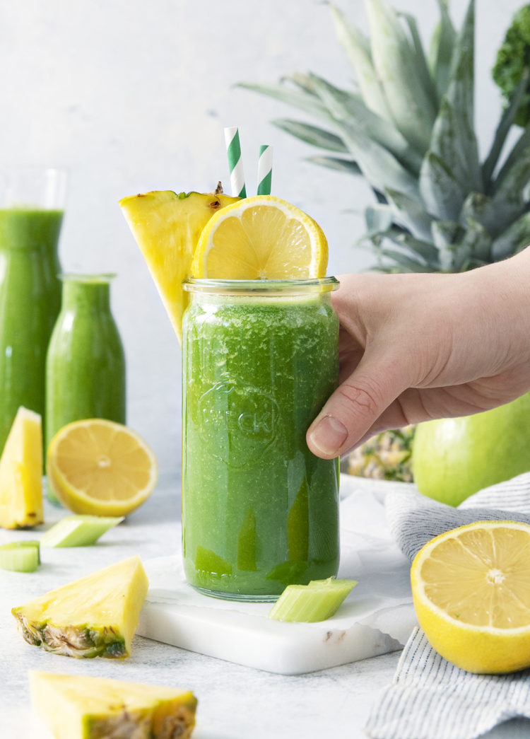 woman picking up a glass of pineapple kale smoothie