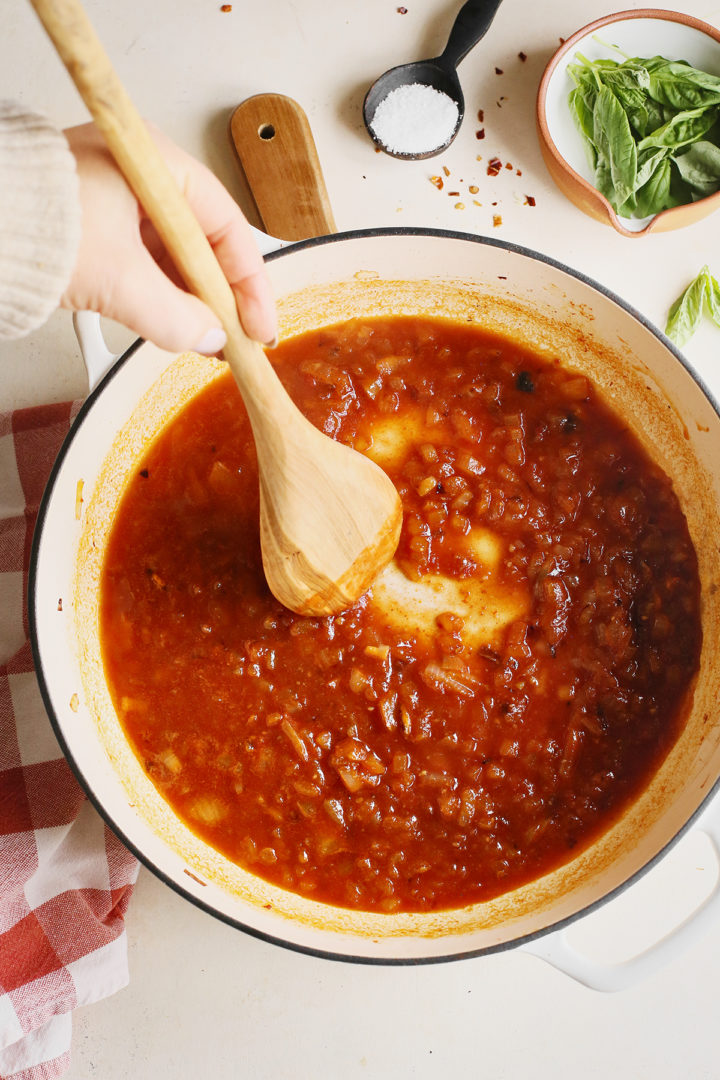 adding tomatoes to vodka sauce cooking in a pan