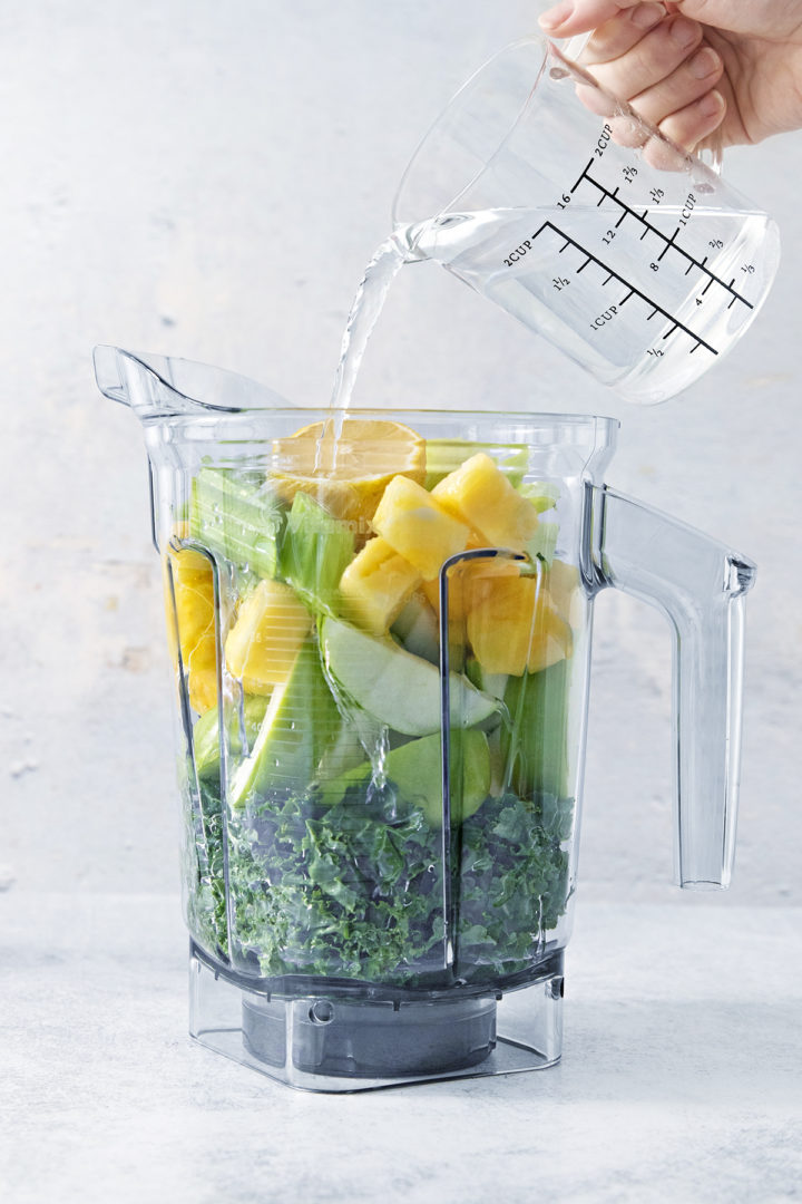 woman adding water to a blender to make a green apple smoothie