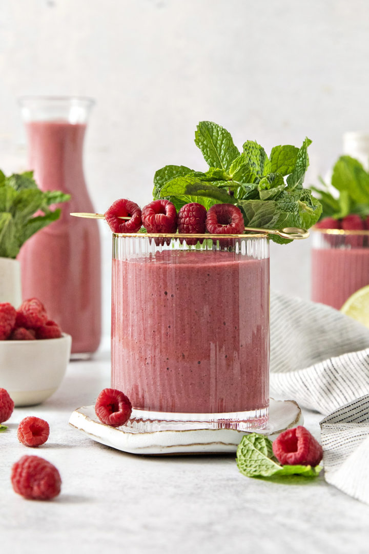 a glass of raspberry banana smoothie garnished with fresh raspberries and mint leaves