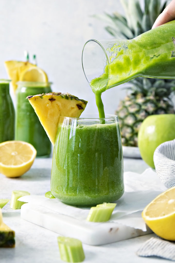 woman pouring pineapple, kale, green apple smoothie into a glass