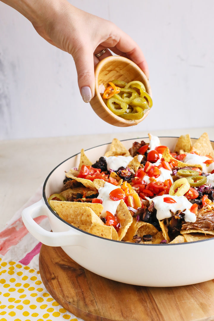 adding sliced pickled jalapenos on to a pan of smoked pork nachos