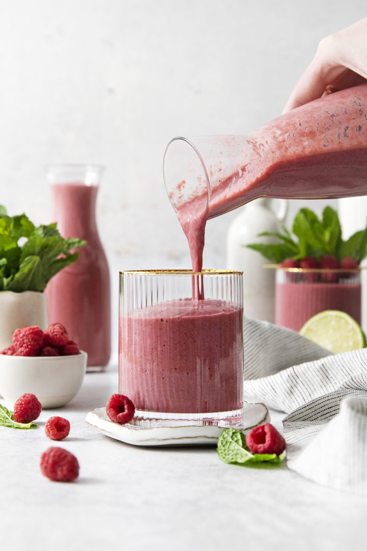 woman pouring a raspberry banana smoothie into a glass