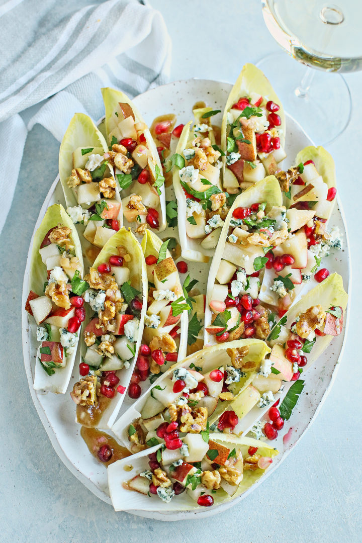 overhead view of stuffed endive appetizers on a platter next to a wine glass