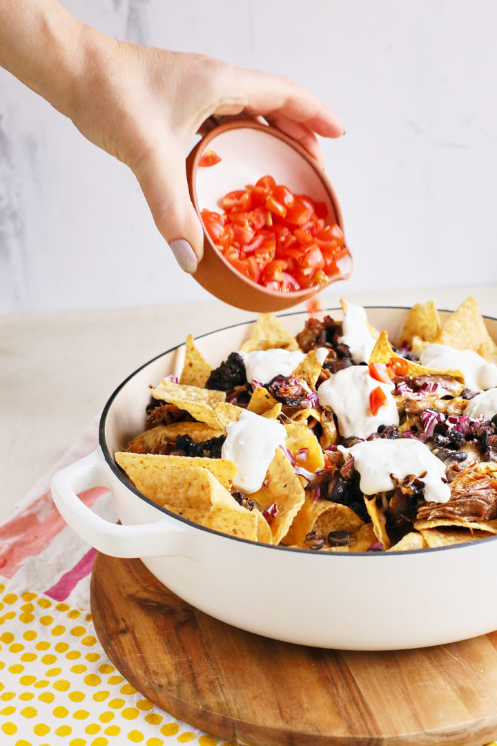 adding pulled pork nachos toppings to a pan of nachos