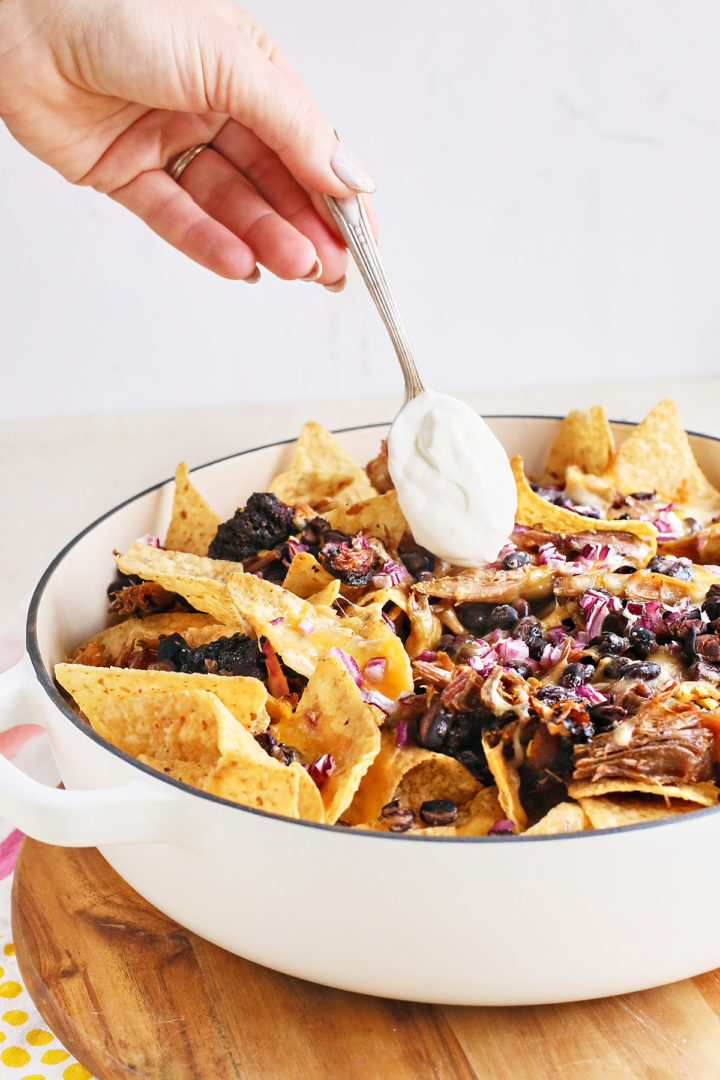 adding lime crema to pulled pork nachos