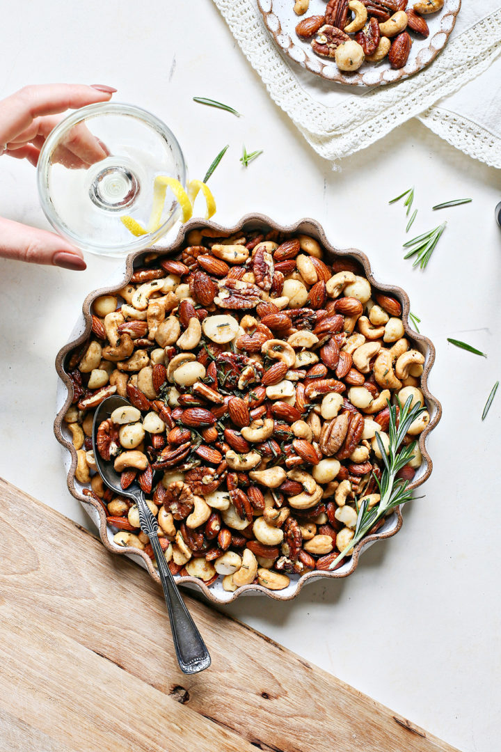 woman picking up a cocktail next to a bowl of sweet and spicy bar nuts