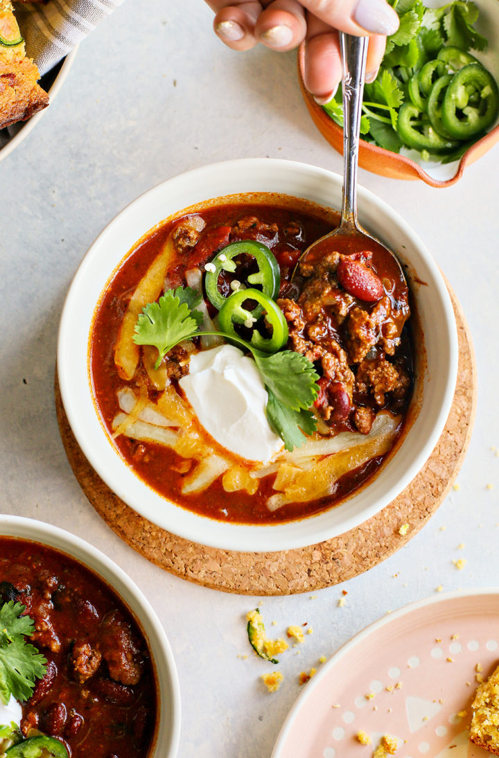 woman scooping ground beef chili in a bowl