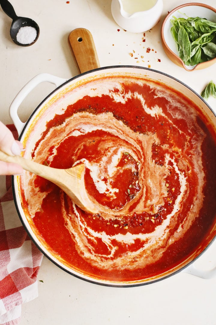 woman stirring cream into a pan of creamy vodka sauce