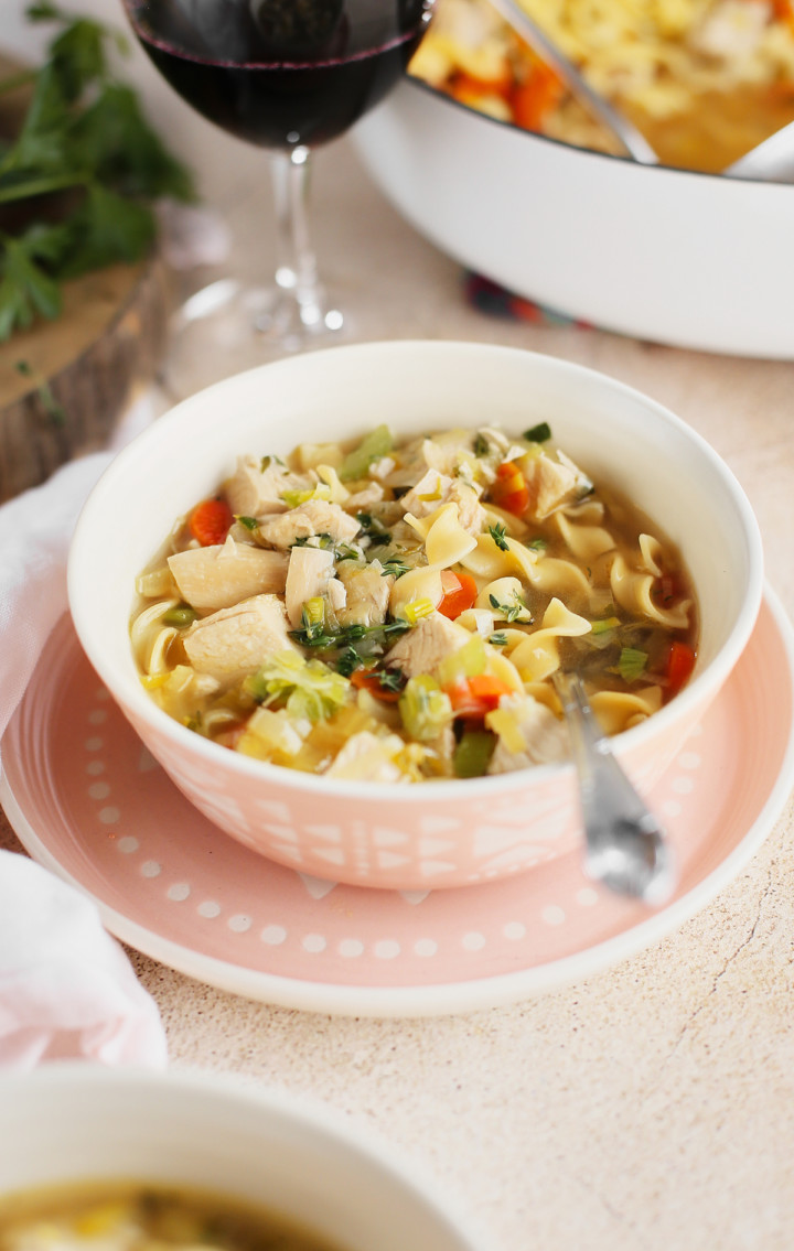 bowl of homemade chicken noodle soup from scratch next to a glass of wine