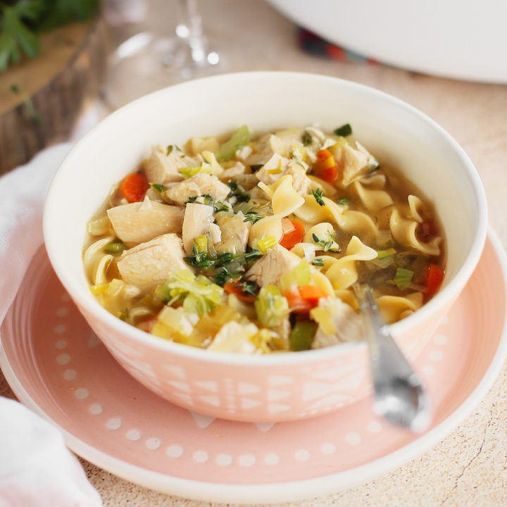 bowl of homemade chicken noodle soup from scratch next to a glass of wine