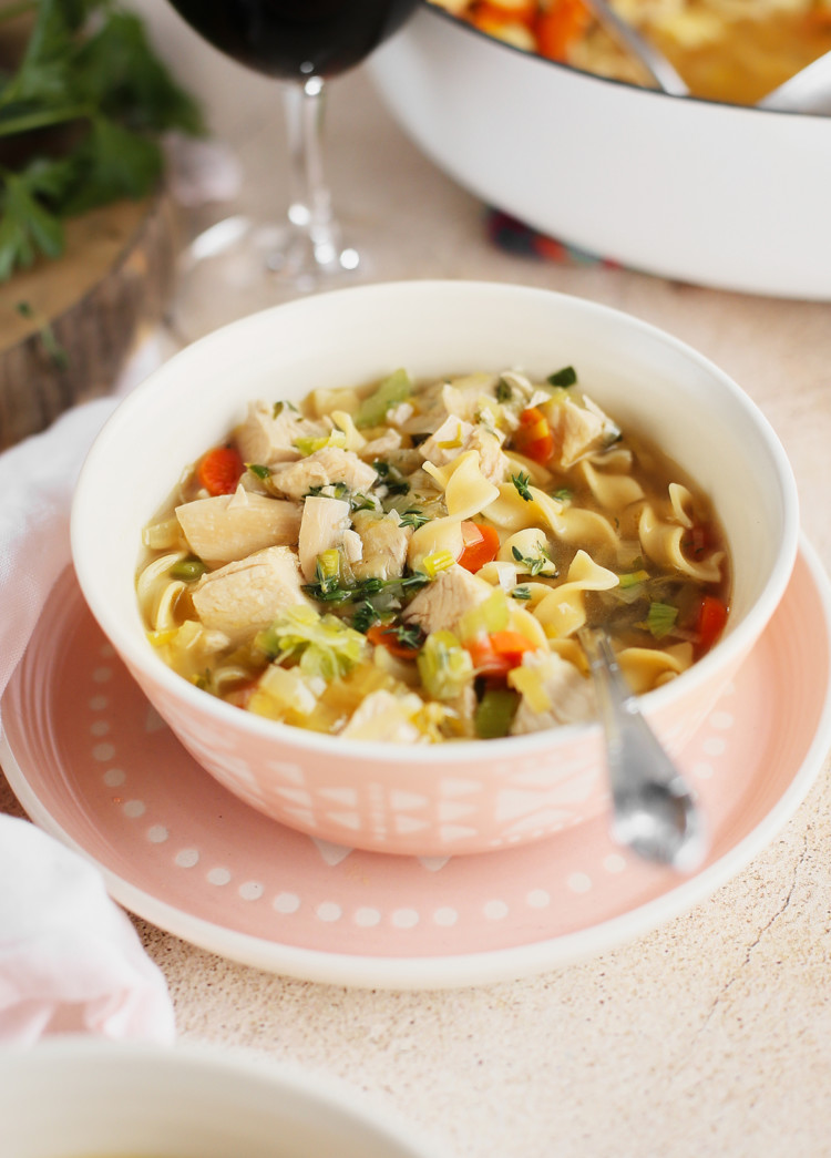 bowl of homemade chicken noodle soup from scratch next to a glass of wine