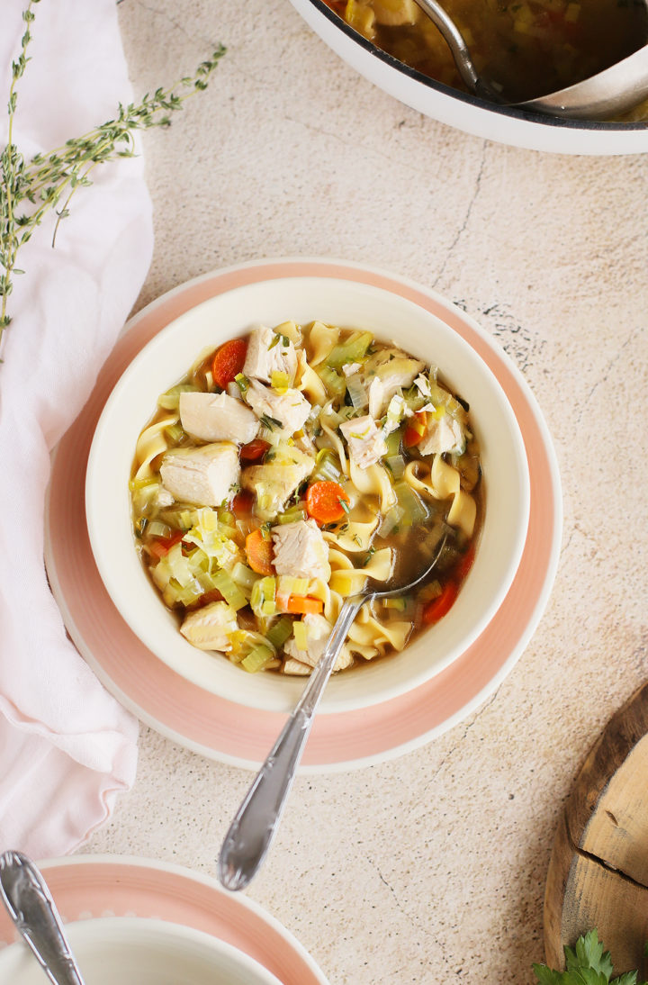 a bowl of homestyle chicken noodle soup with a spoon next to fresh thyme