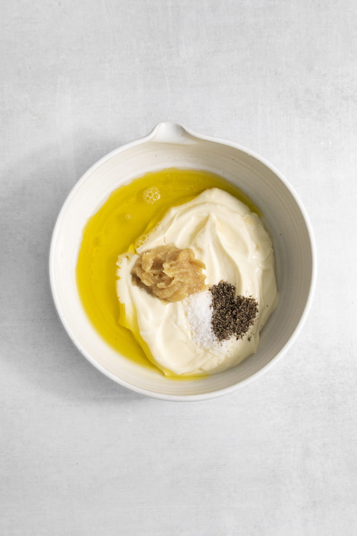 ingredients for roasted garlic aioli in a bowl: olive oil, mayonnaise, roasted garlic, lemon juice salt, and pepper