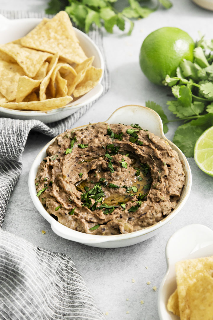 black bean hummus served in a white bowl next to tortilla chips and fresh cilantro