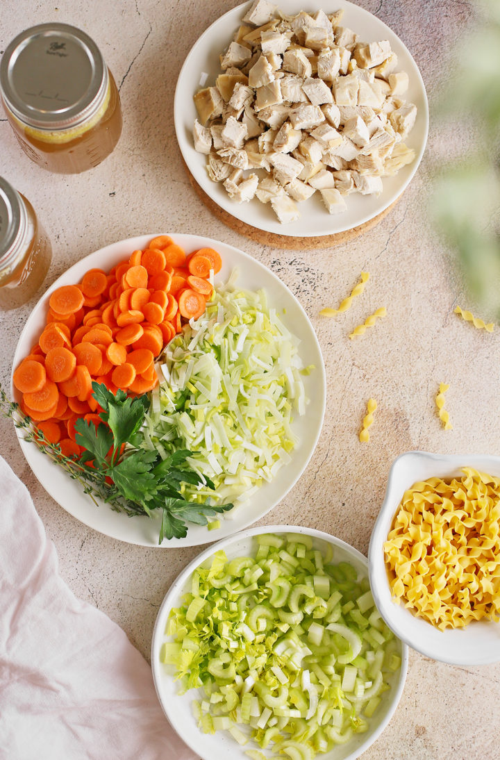 an arrangement of the ingredients in hearty chicken noodle soup on a stone background
