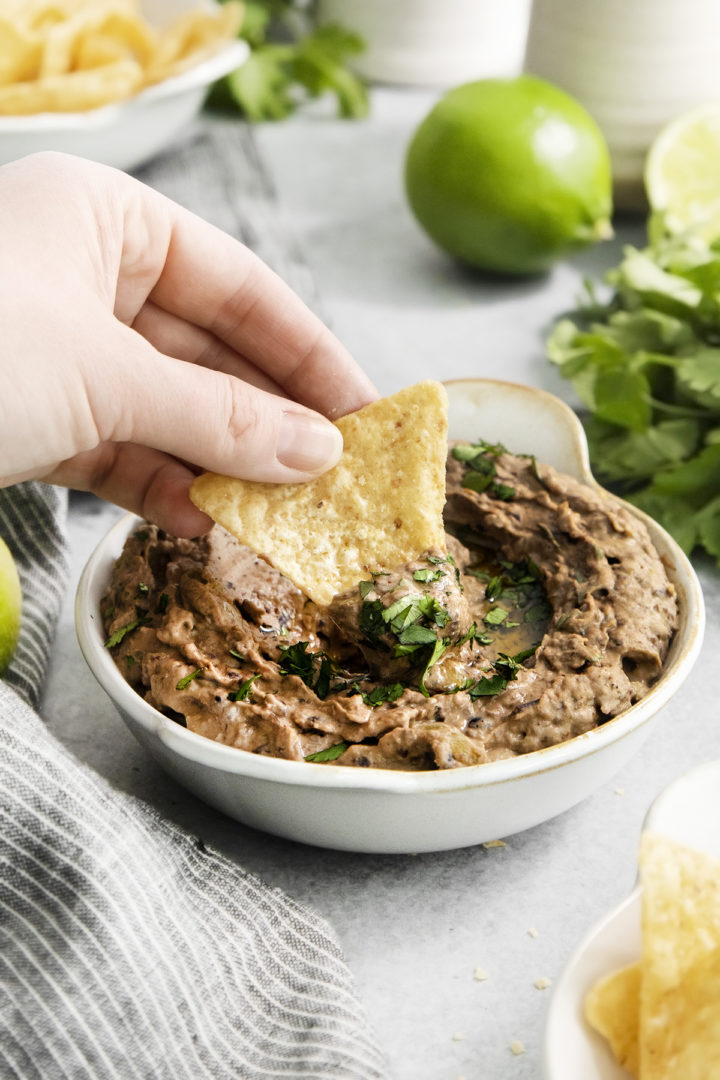woman scooping black bean dip with a tortilla chip