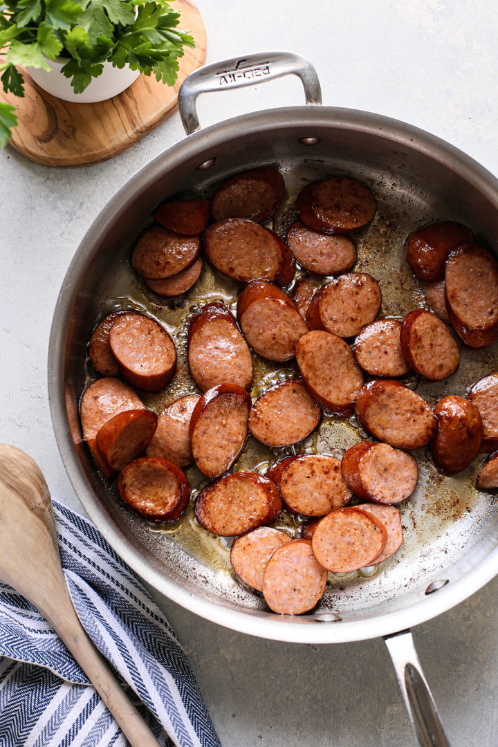 andouille sausage cooking in a stainless steel pan for a red beans and rice recipe