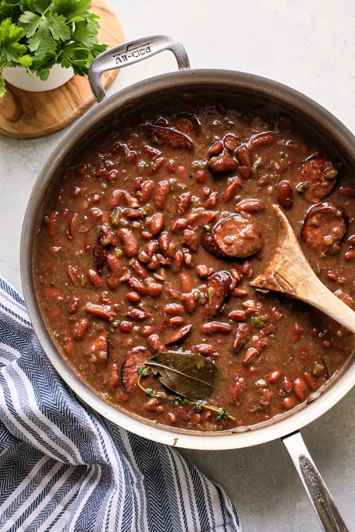 wooden spoon stirring a pot of red beans with andouille sausage