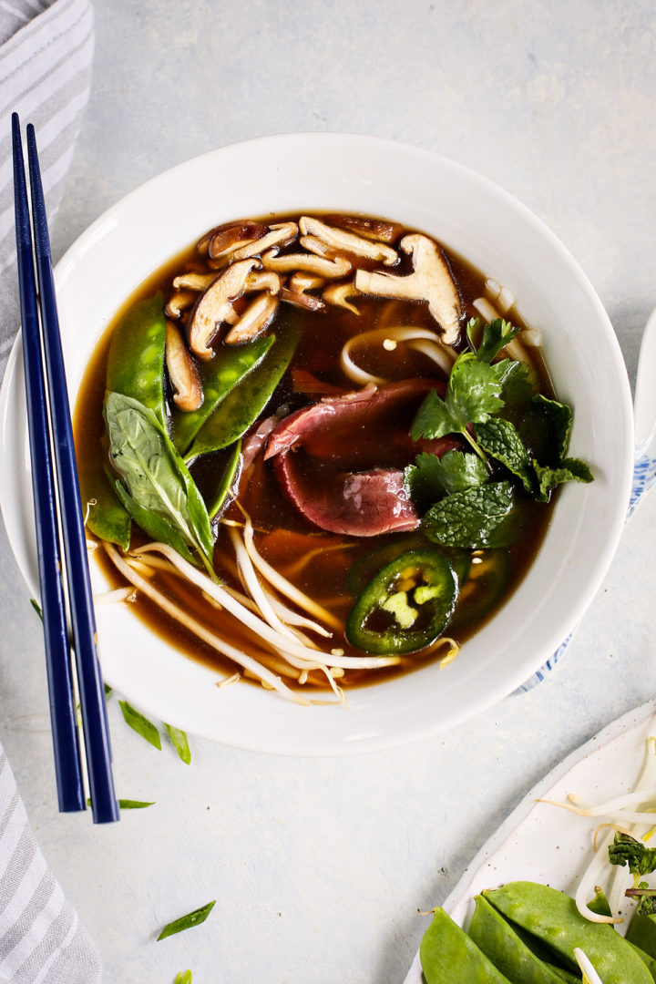 vietnamese beef noodle soup in a white bowl garnished with fresh herbs