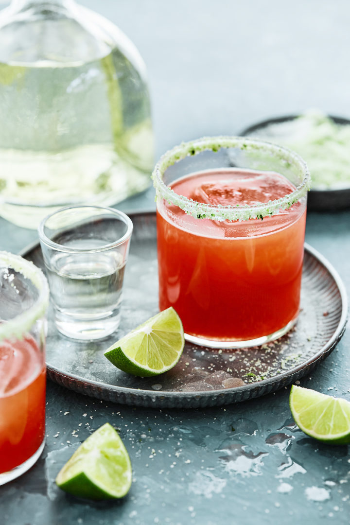 margarita in a glass next to tequila and limes for national margarita day celebration