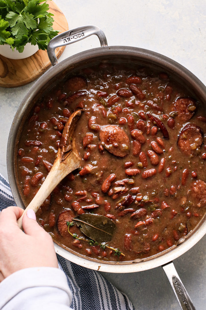 woman stirring andouille sausage and red beans with a wooden spoon