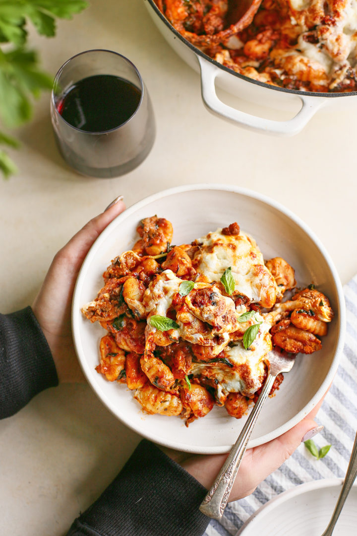 woman holding a plate of Cheesy Italian Sausage Gnocchi Bake