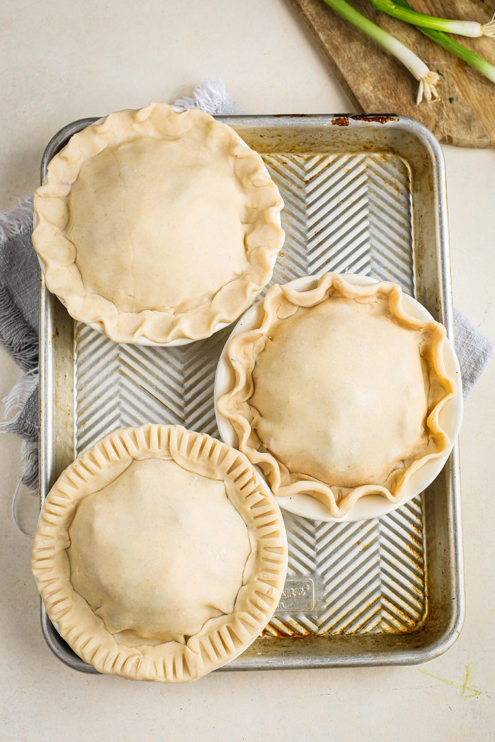 three mini pot pies on a baking sheet ready to go in the oven