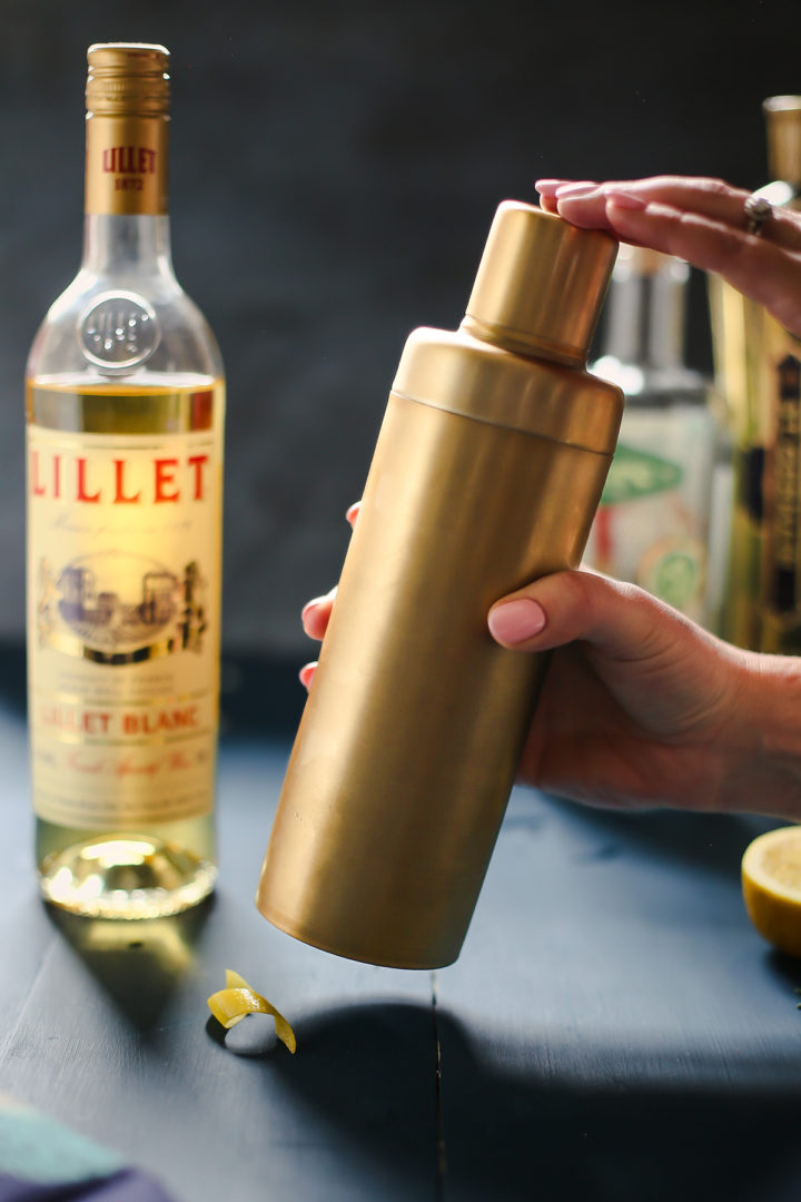 woman shaking ingredients in for a french blonde in gold cocktail shaker
