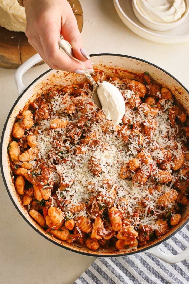 woman adding ricotta cheese on top of gnocchi with red sauce