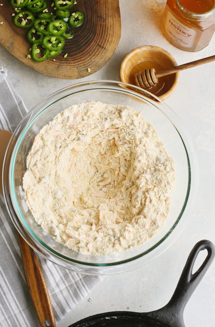 dry ingredients for cornbread with jalapenos in a glass bowl next to a cast iron skillet