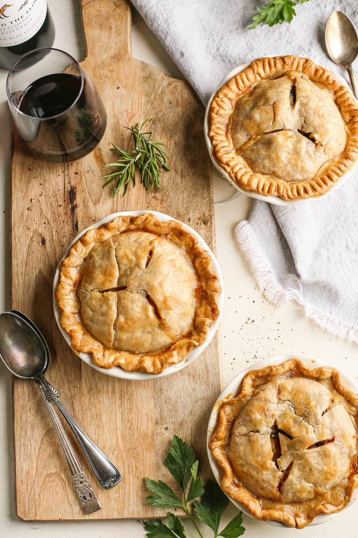 three mini chicken pot pies on a wooden cutting board with a glass of red wine