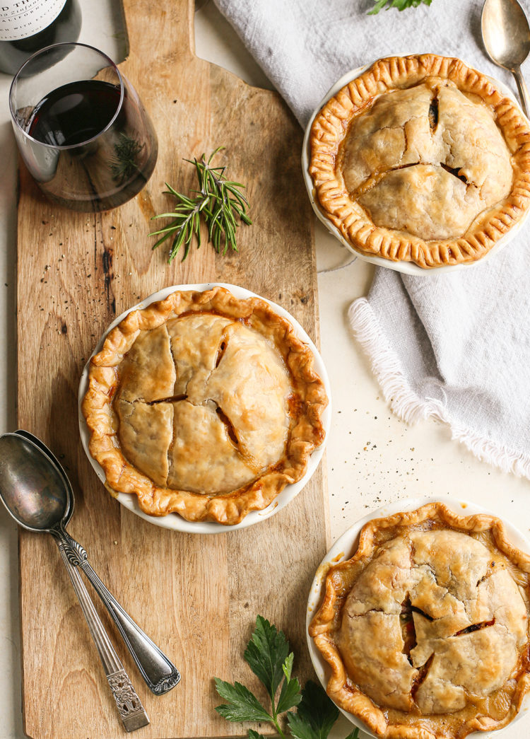 3 mini chicken pot pies on a wooden cutting board with a glass of red wine