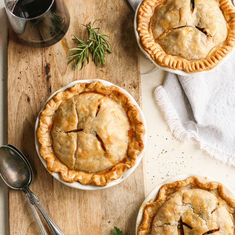 3 mini chicken pot pies on a wooden cutting board with a glass of red wine