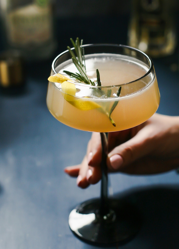 woman holding a glass of a french blonde cocktail with a rosemary garnish
