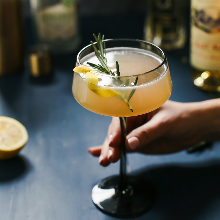 woman holding a glass of a french blonde cocktail with a rosemary garnish