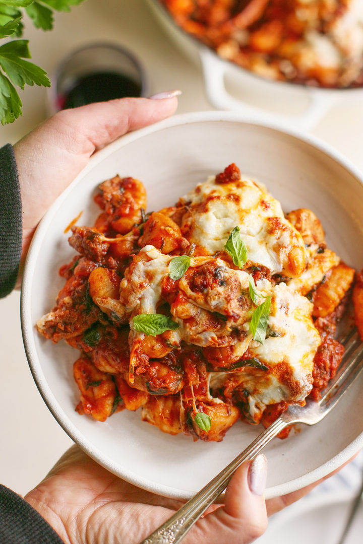 woman holding a plate with a serving of baked gnocchi on it