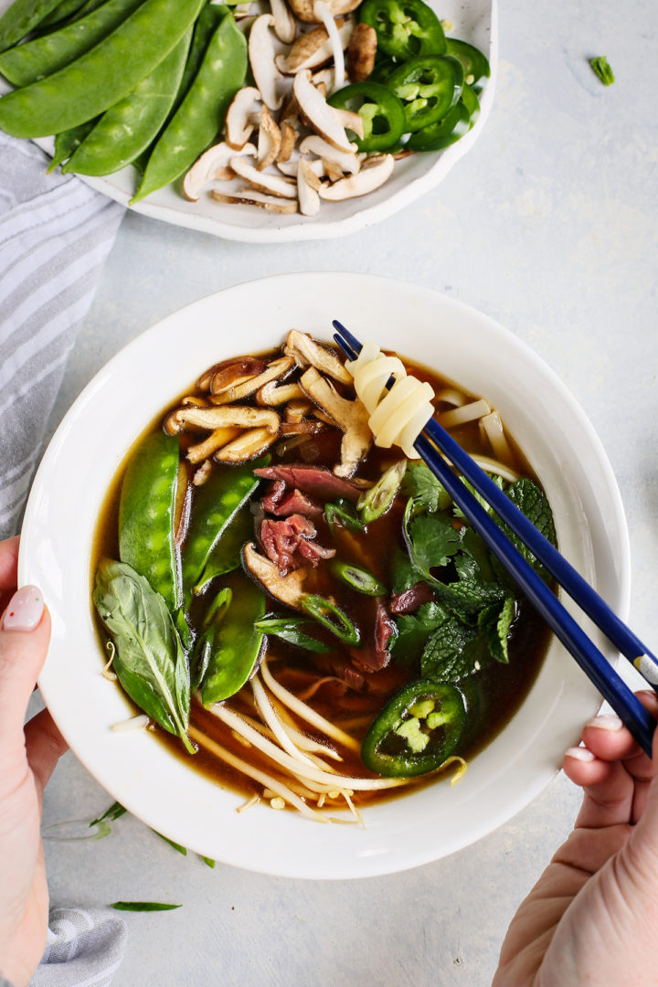 woman eating a bowl of vietnamese beef noodle soup with blue chopsticks 