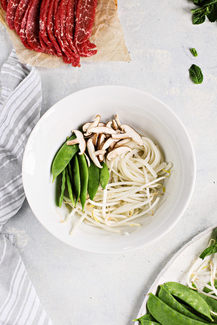 vietnamese rice noodles and vegetables in a white bowl next to thinly sliced beef	