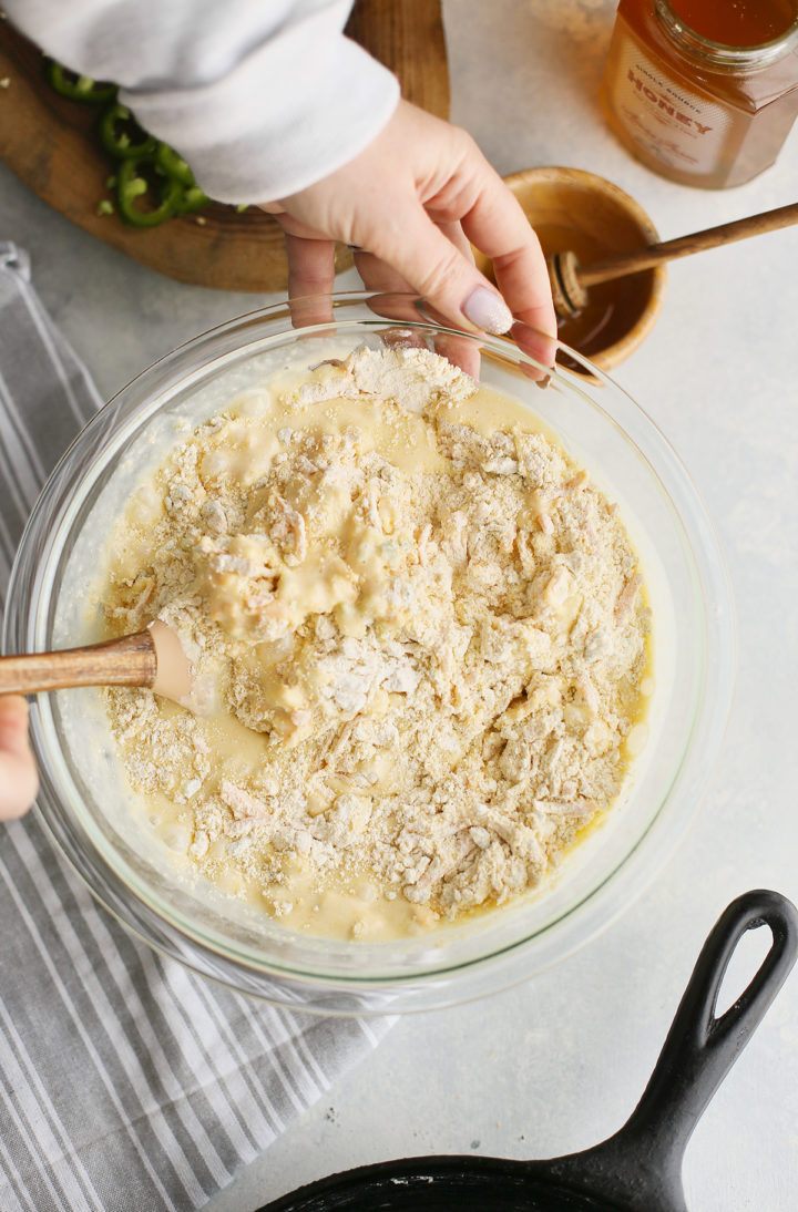 woman stirring liquid ingredients to dry ingredients to make batter for cornbread with jalapenos