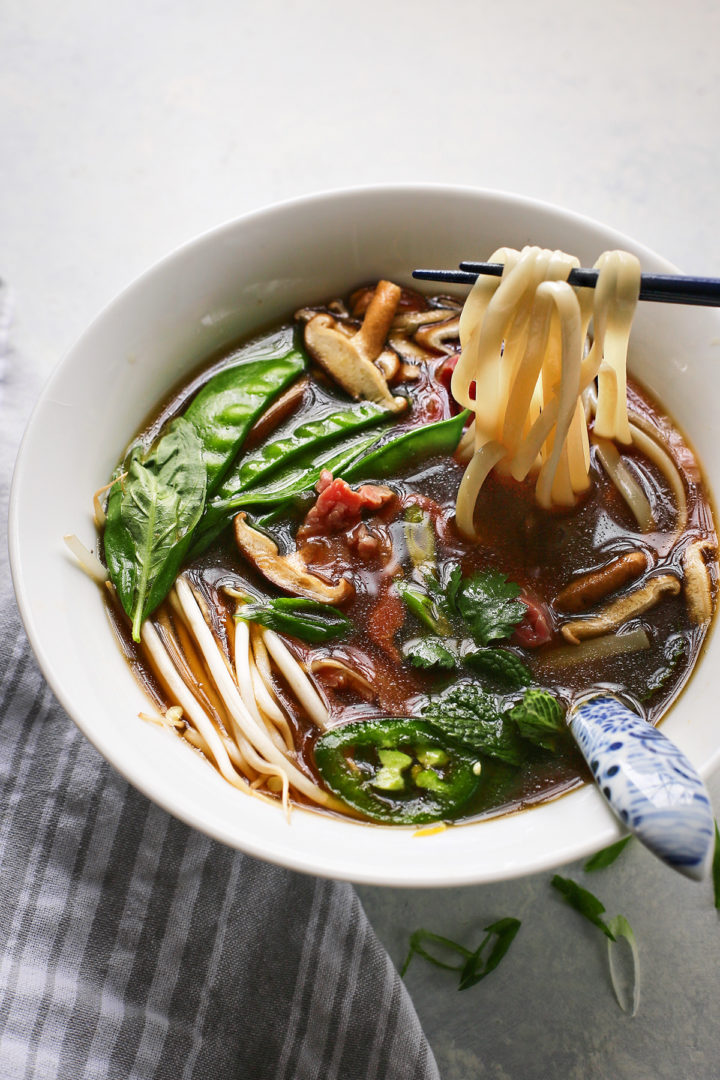 Vietnamese soup with rice noodles, beef, and vegetables in a white bowl