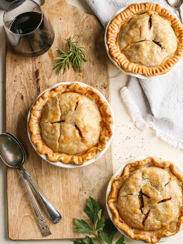 3 mini chicken pot pies on a wooden cutting board with a glass of red wine