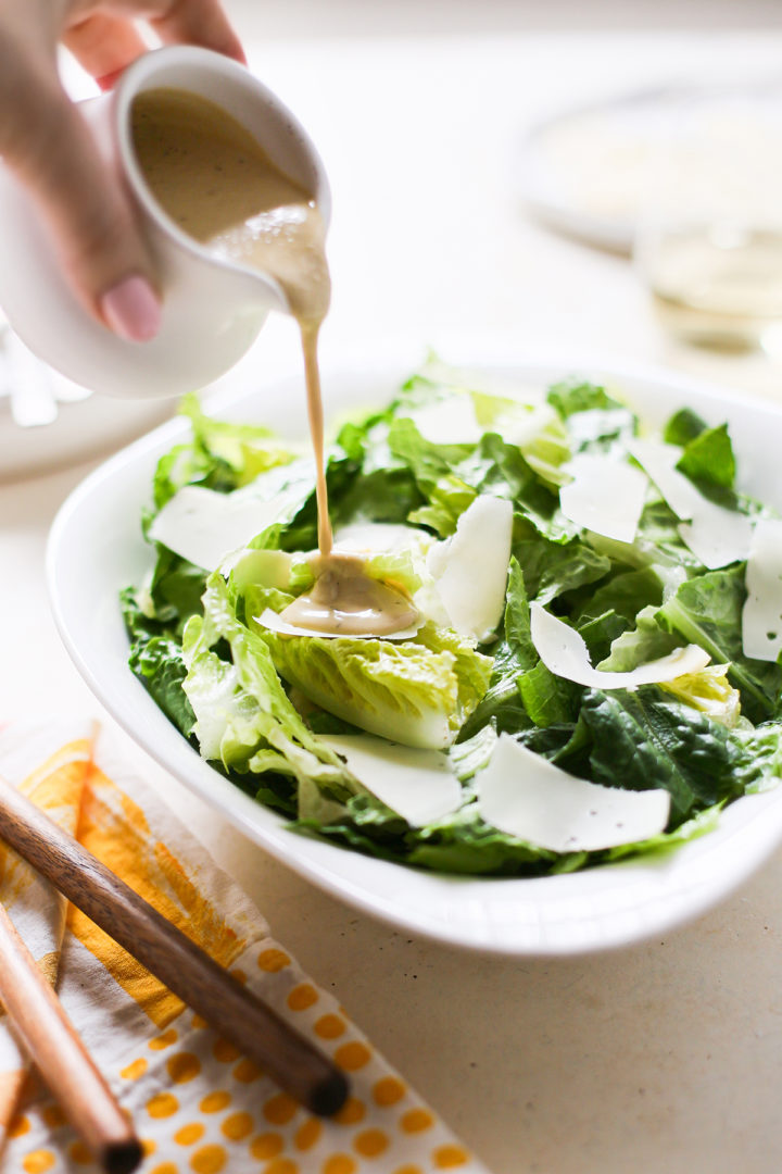 woman pouring homemade caesar dressing on top of salad