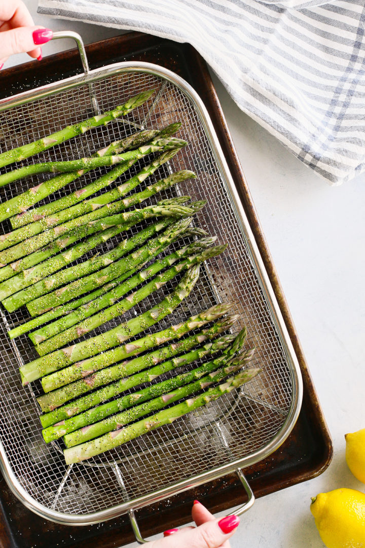 woman holding a wire grill pan with seasoned fresh asparagus to make pellet grilled asparagus