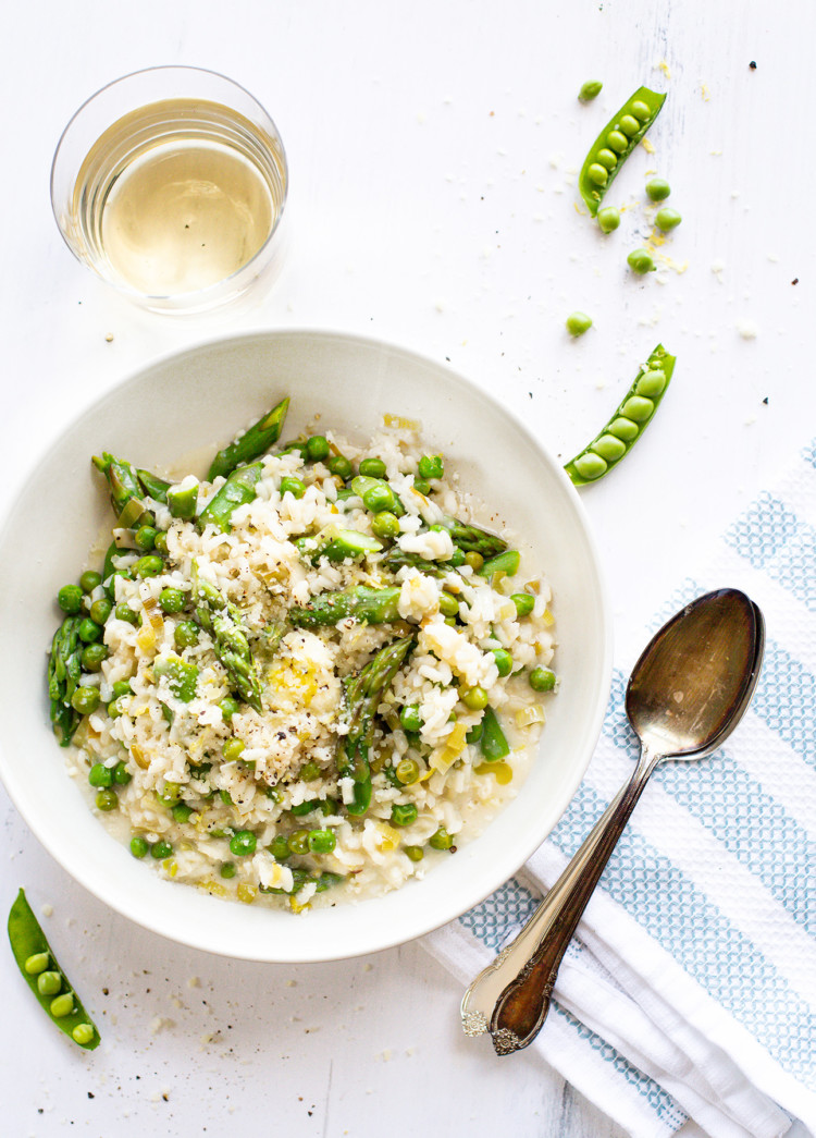 overhead photo of asparagus risotto in a white bowl with a glass of white wine