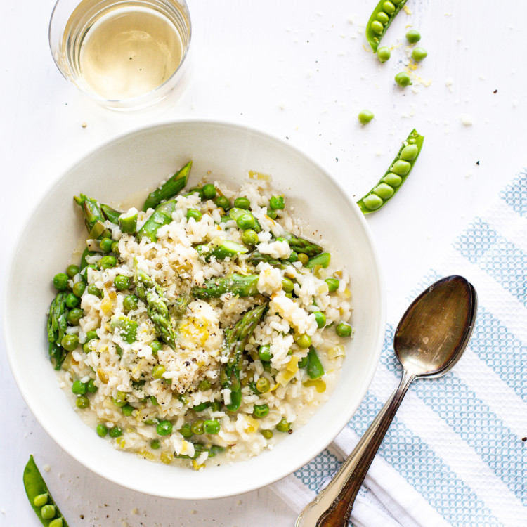 overhead photo of asparagus risotto in a white bowl with a glass of white wine